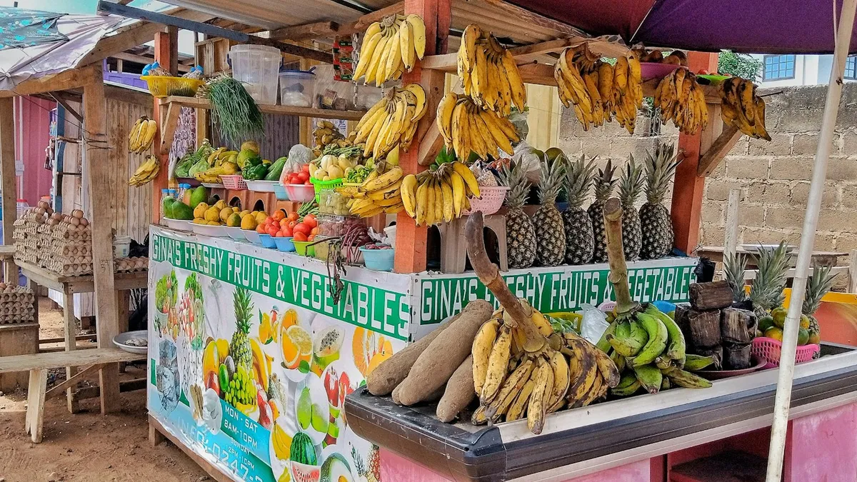 Étal de fruits et légumes au Ghana, avec ignames, bananes plantain, ananas et régimes de bananes