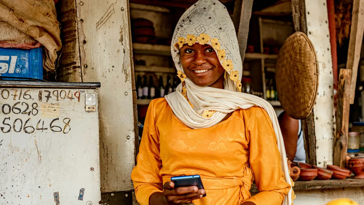 Commerçante souriante, téléphone en main, derrière l'étal de fruits de sa petite boutique