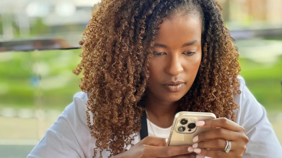 Femme aux cheveux bouclés consultant son smartphone, le regard concentré sur l'écran