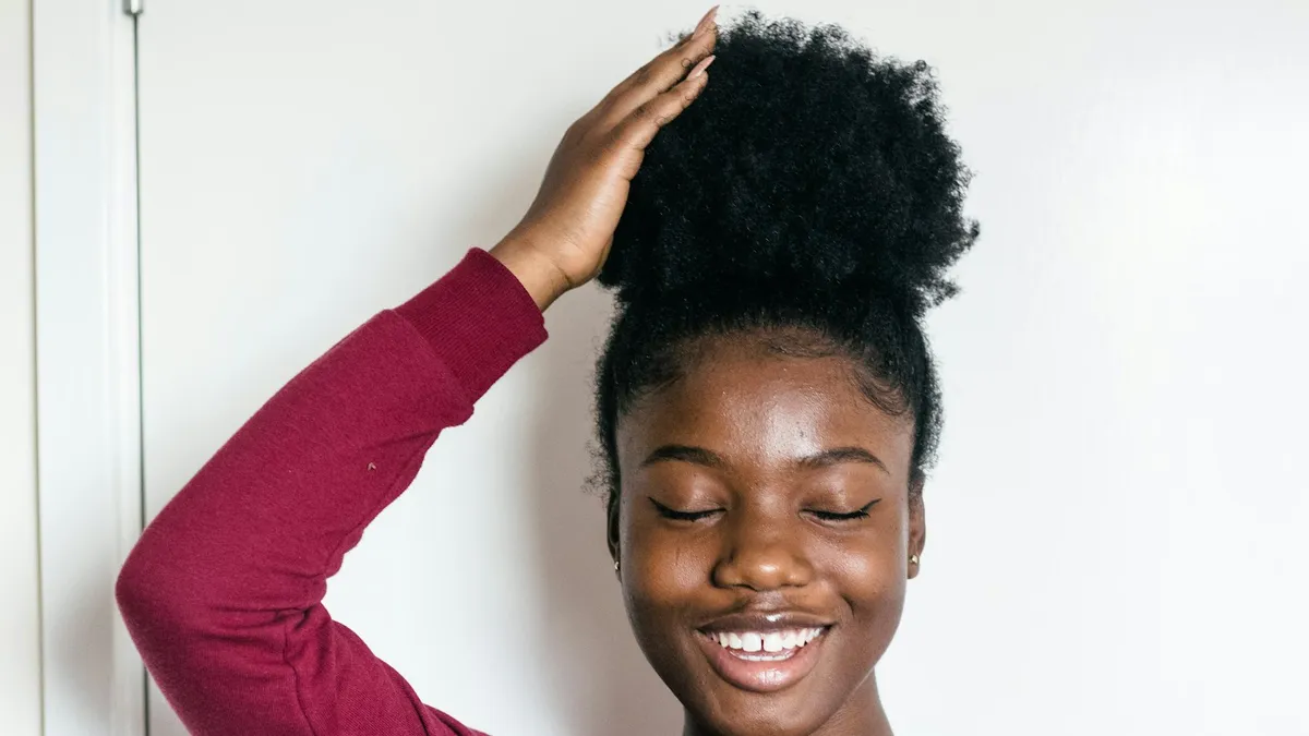 Jeune femme souriante, la main posée sur ses cheveux crépus naturels coiffés en chignon