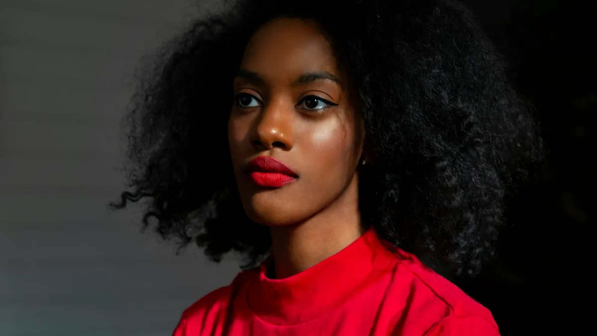 Portrait de profil d'une femme aux cheveux crépus naturels, en pull rouge, sur fond sombre