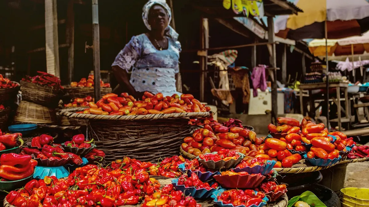 Vendeuse derrière des paniers de piments frais sur un marché en plein air