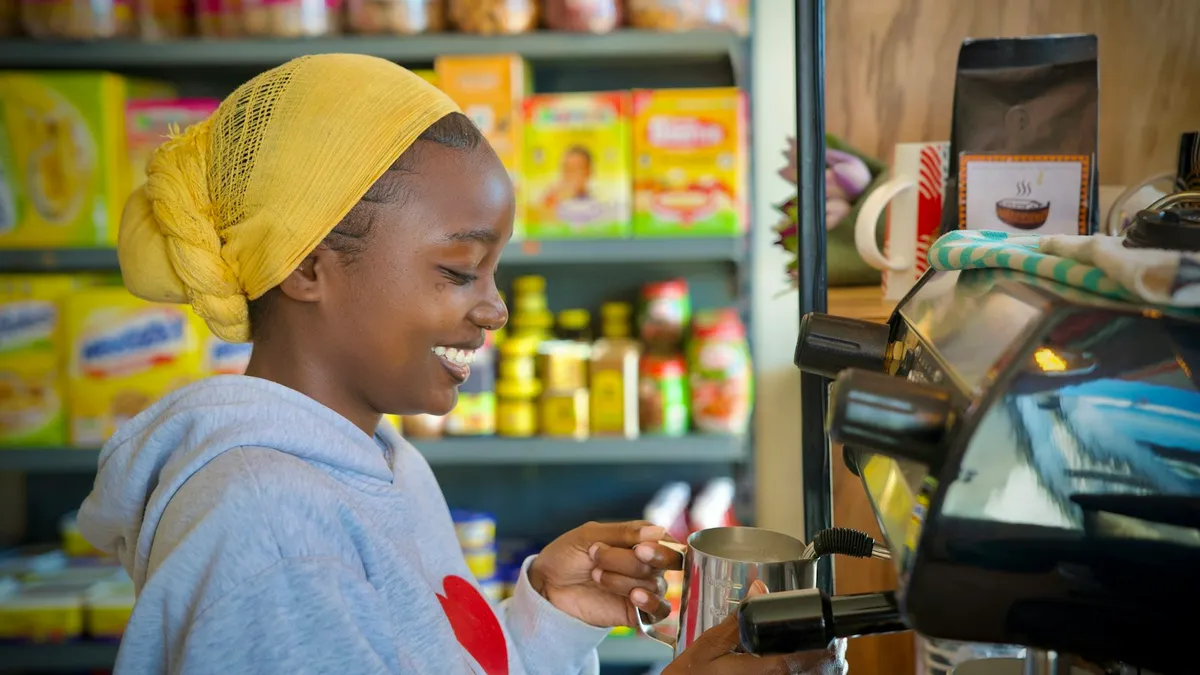 Jeune femme souriante qui prépare un café derrière le comptoir d'un petit commerce de quartier