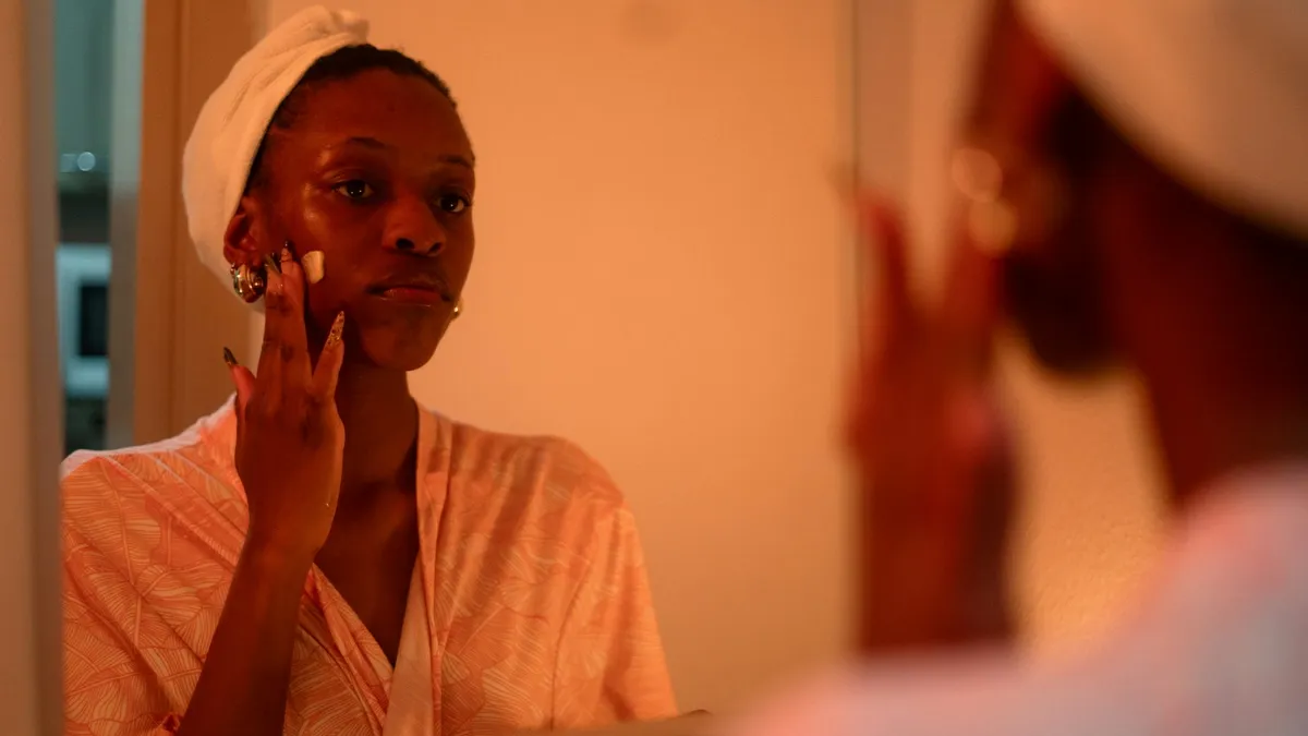Femme en peignoir appliquant une crème sur son visage devant un miroir