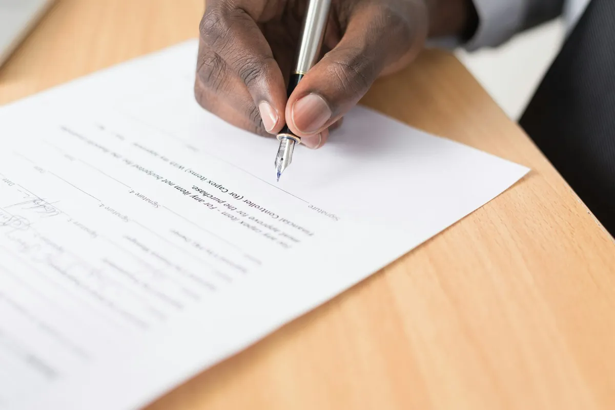 Main qui signe un document au stylo plume sur un bureau en bois clair