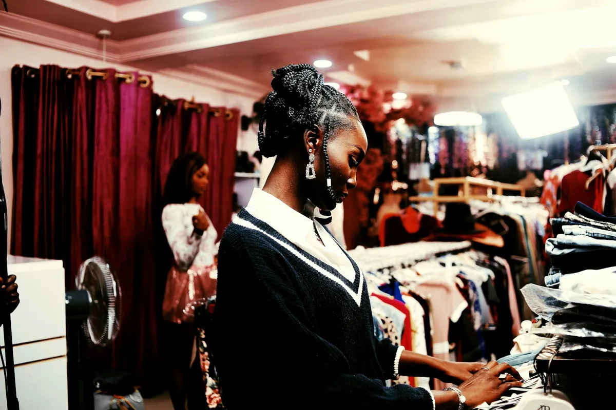 Jeune femme aux tresses qui choisit un vêtement sur un portant, dans une boutique de mode