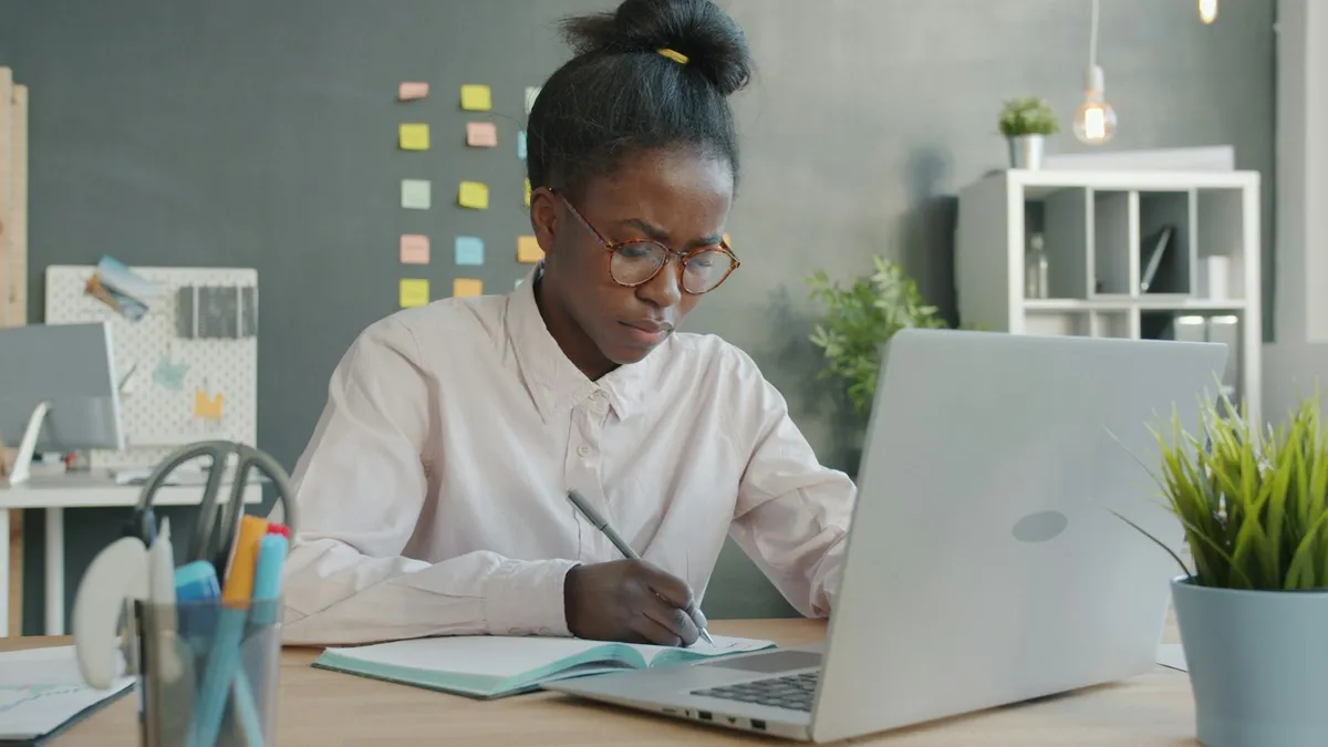 Femme qui note ses observations dans un carnet à côté de son ordinateur portable