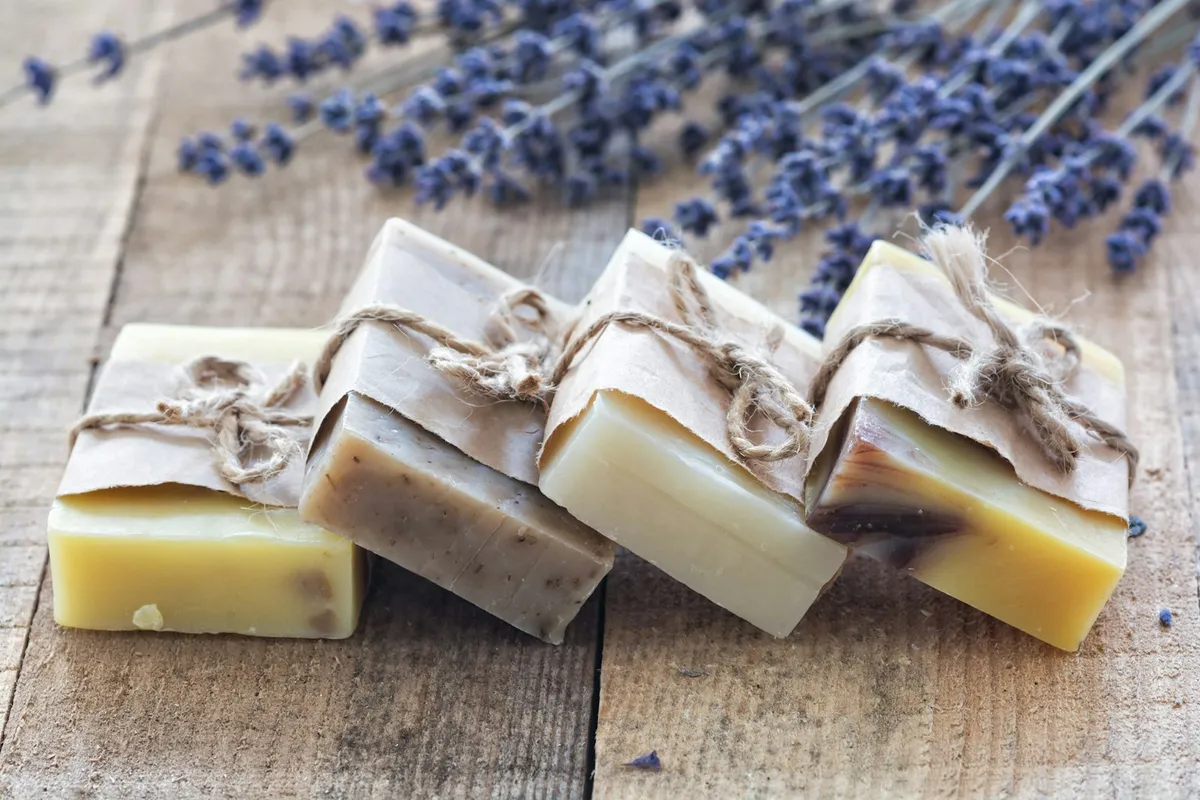 Quatre savons artisanaux emballés dans du papier kraft et noués de ficelle, sur une table en bois avec des brins de lavande