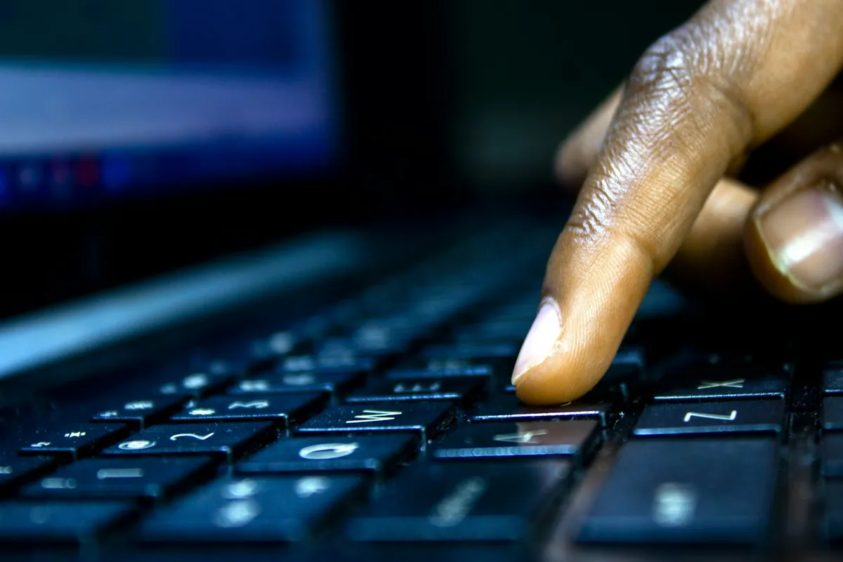 Doigt qui appuie sur une touche du clavier d'un ordinateur portable, écran allumé en arrière-plan