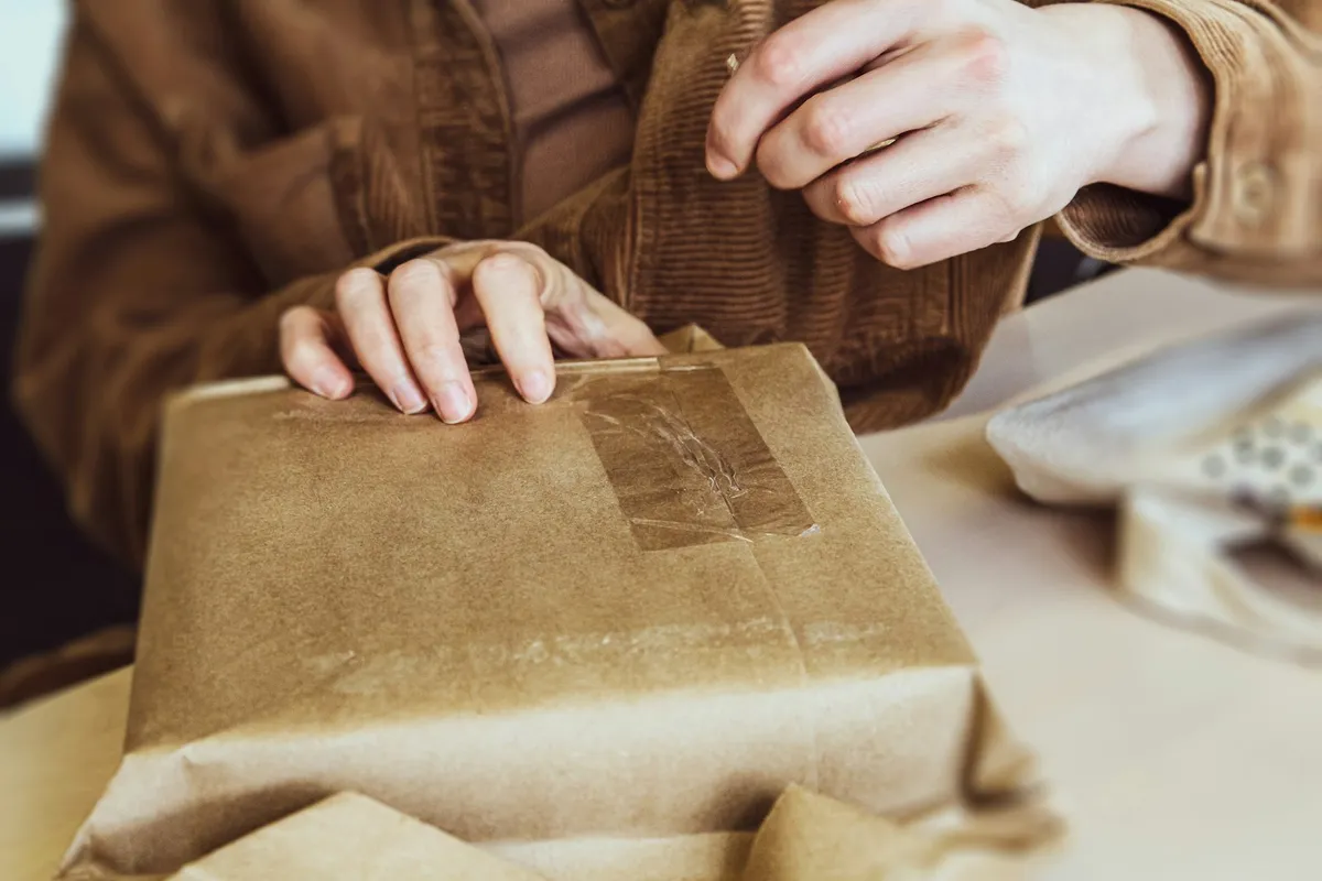 Mains qui emballent un colis en papier kraft sur une table avant son expédition